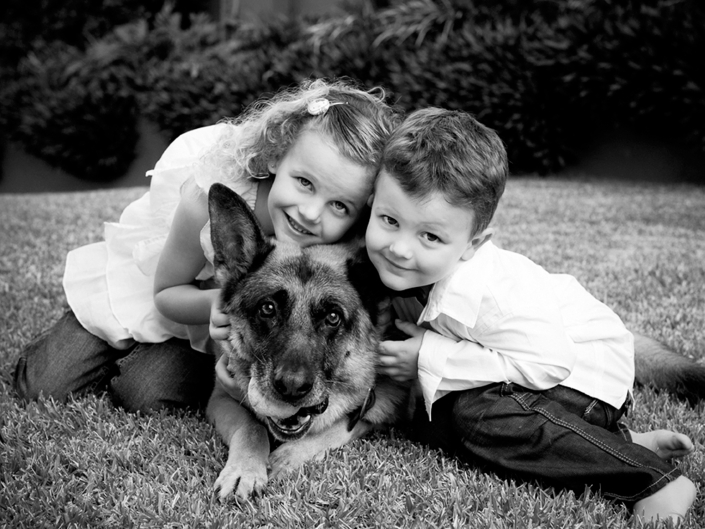 little boy and girl with german shepherd dog pet wearing white shirts sitting on grass