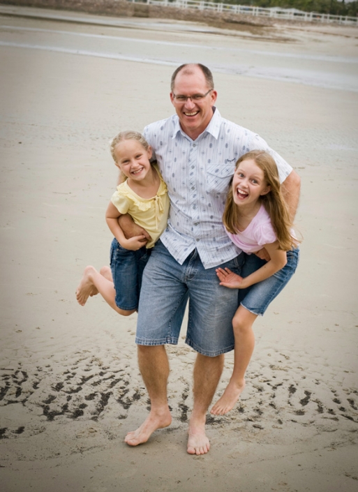 Dad holds two daughters on sandy beach having fun