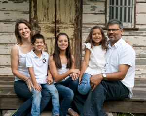 Family of 5 wears white shirts and jeans for family photography with rustic tin shed background
