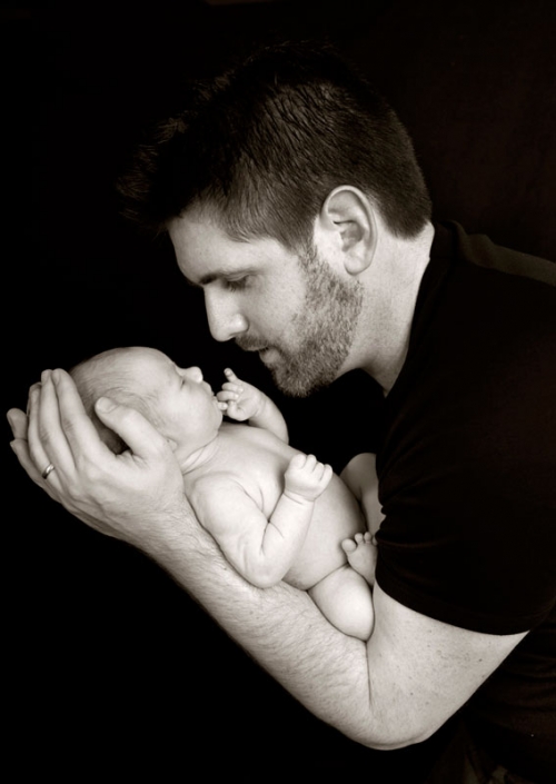 father holds newborn baby in arms close to face