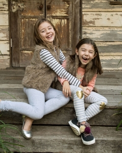 sisters laughing wearing winter clothing sitting in fornt of rustic tin shed