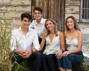 lovely family with Mother and two teenage sons and one teenage daughter wearing white and denim in front of rustic tin shed