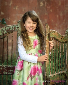 sweet little girl wearing floral dress smiles standing in antique gates