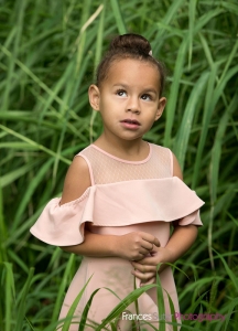 stunning little girl wearing pretty pink dress posing in long grass for photograph