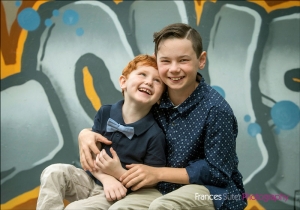 young brothers share a laugh sitting in front of graffiti wall wearing button up shirts and bow tie