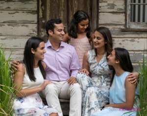 family wearing pastel coloured clothing posing for family portrait image in front of rustic tin shed backdrop