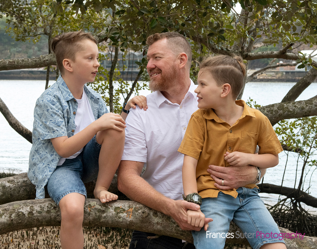 Father and two teenage sons sitting casually on tree branch at beach in Brisbane City
