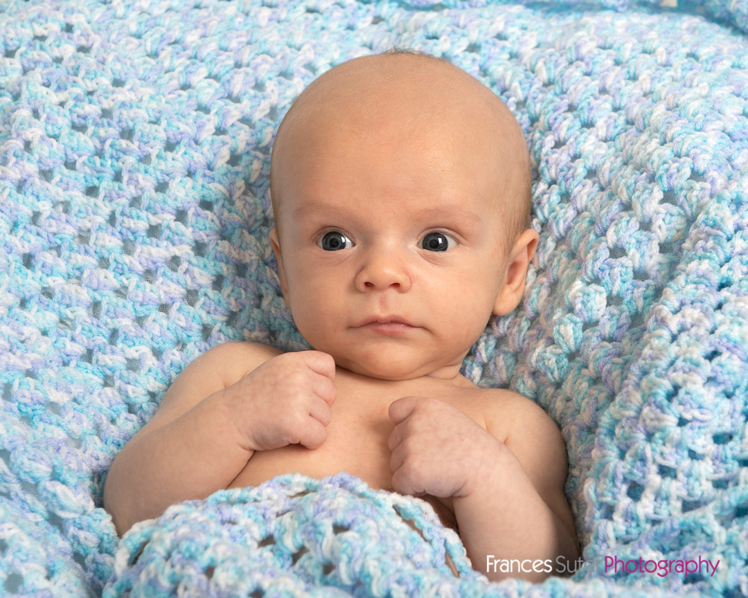 newborn baby lays in blue hand knitted baby blanket at family photoshoot