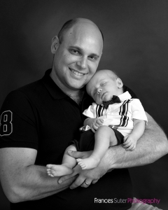 Proud Father smiles while holding his sleeping newborn son in his arms photograph in black and white