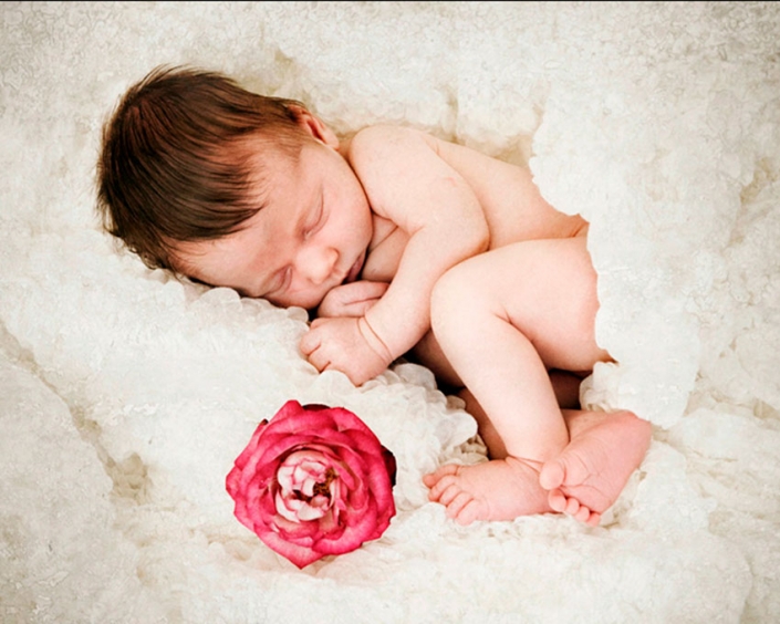 newborn sleeping next to pink flower